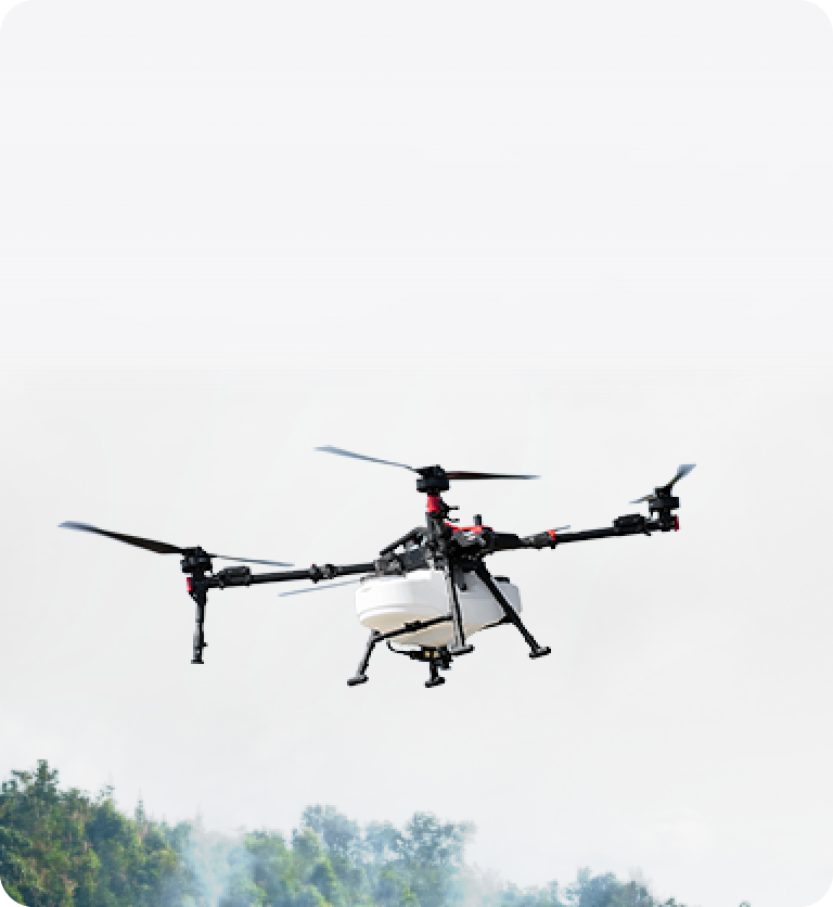 A quadcopter drone is flying outdoors above some trees, with a clear sky in the background.